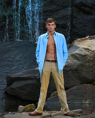 senior picture of louisville kentucky graduate. boy in blue shirt and khaki pants standing in front of a waterfall