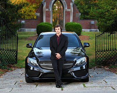 senior picture of louisville kentucky graduate. boy in black suit leaning against his black car