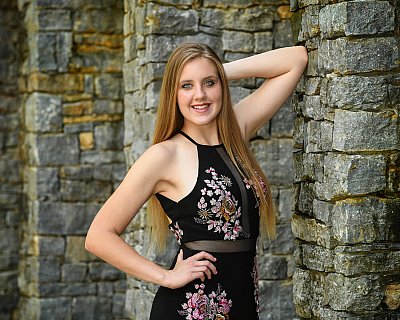 senior photography of louisville kentucky graduate. girl in black flower dress posing next to rock wall