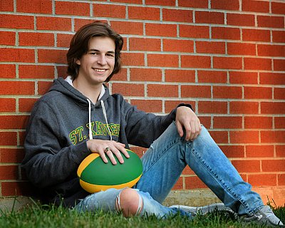 senior photography of louisville kentucky graduate. teenage boy sitting and leaning on brick wall holding a green and yellow football