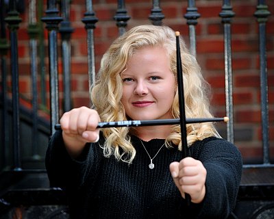 senior photography of louisville kentucky graduate. teenage girl with blonde hair wearing black shirt holding out drumsticks 
