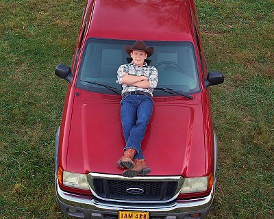 senior photography of louisville kentucky graduate. teenage boy wearing cowboy hat laying on red car