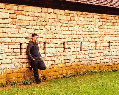 senior photography of louisville kentucky graduate. teenage boy leaning against stone wall wearing all black, brown hair