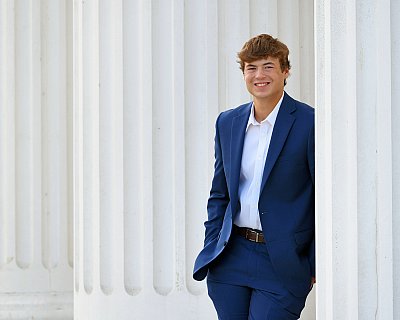 senior photography of louisville kentucky graduate. teenage boy with brown hair in navy suit, standing next to white columns
