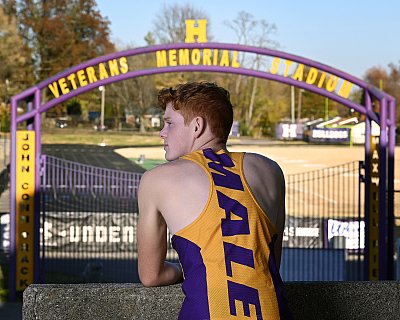 senior photography of louisville kentucky graduate. teenage boy with red hair showing off the back of his yellow and purple track athletic uniform