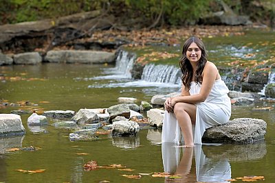 senior photography of louisville kentucky graduate.  teenage girl in white dress, sitting on a rock in a stream