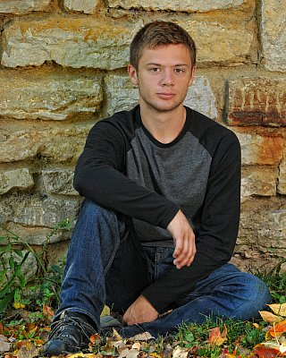 senior photography of louisville kentucky graduate. teenage boy in black shirt and blue jeans posing in front of stone wall