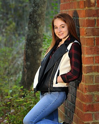 senior photography of louisville kentucky graduate. girl with red hair and white vest leaning against brick wall