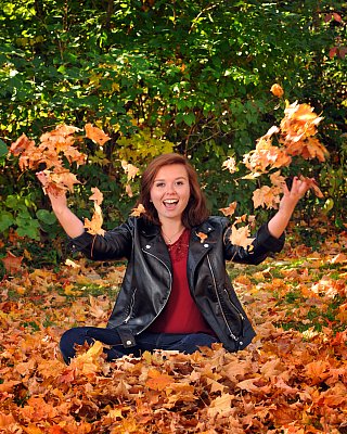 senior photography of louisville kentucky graduate. teenage girl with red hair sitting in leather jacket throwing fall leaves