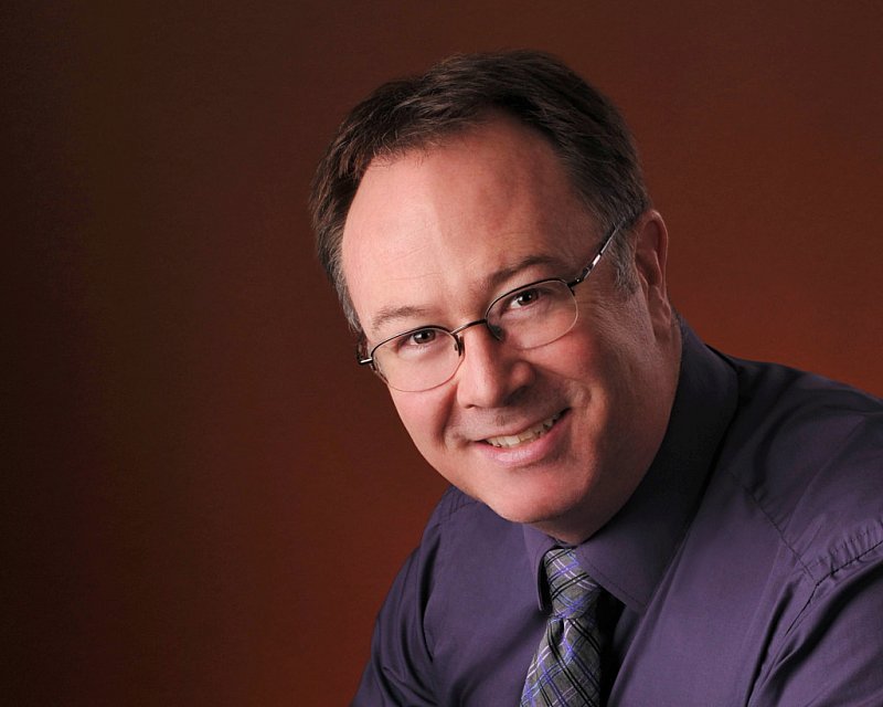 headshot of craig davis, owner of craig davis photography in lousiville, ky. specialist in senior pictures. red background, purple shirt, brown hair