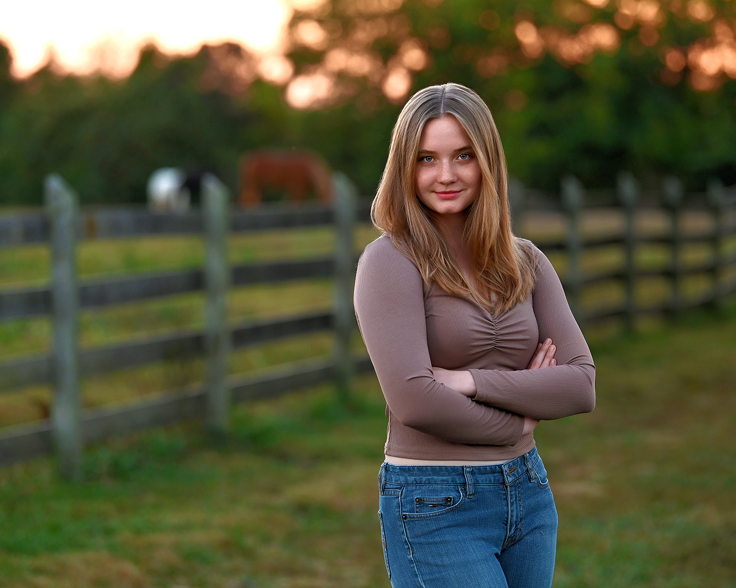 senior picture of louisville kentucky graduate. girl with brown hair, brown shirt, out in pasture, horses in background